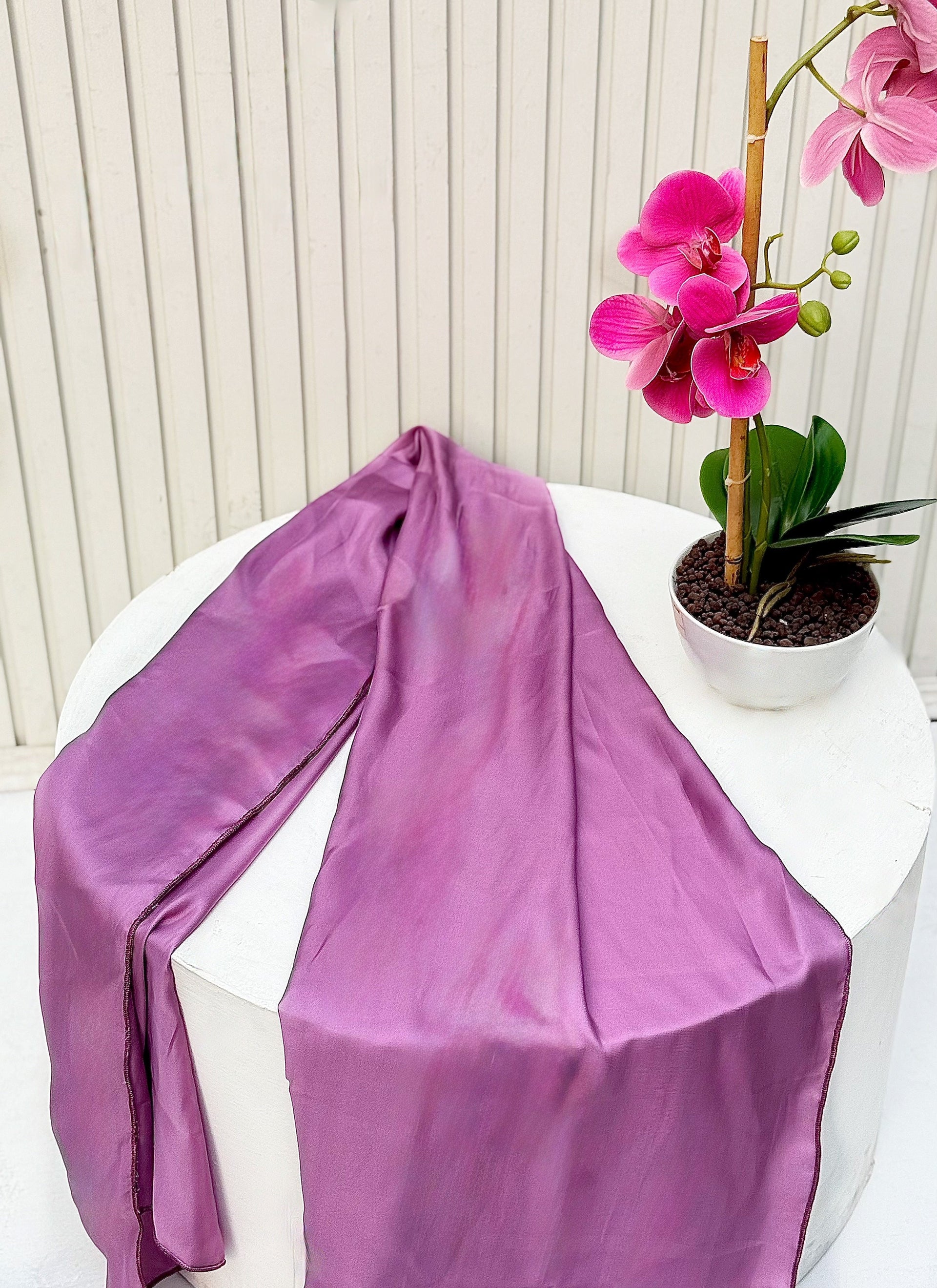 Elegant purple silk scarf displayed beside vibrant pink orchids.
